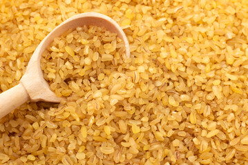Bulgur wheat background. Bulgur grains lie in a wooden spoon. View from above