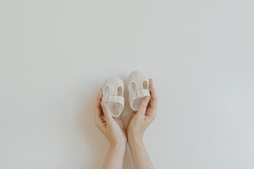 Person's hands hold cute little baby sandals shoes on white background. Minimalist baby fashion...