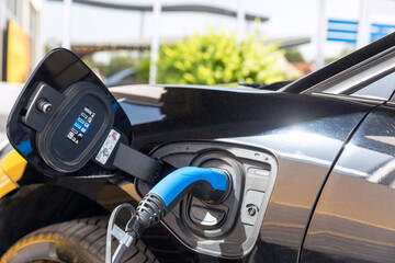 Electric car with plug-in socket at charge station charging battery