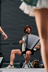 vertical photograph of a young man with a bearded musician playing accordion on a tourist street in...