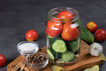 Cucumbers and cherry tomatoes are placed in jar with garlic, bay leaves, pepper and dill. Preparation for pickling