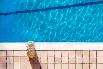 top view of a woman with a hat on the edge of a pool with blue water. horizontal format. relax and...