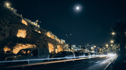 Trails of car headlights driving by enlightened caves carved inside of rock formation. Ancient...