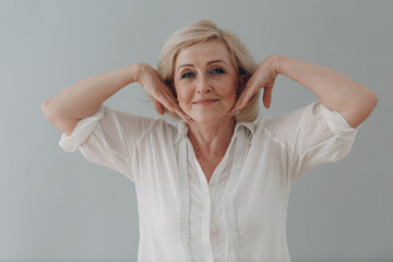 Elderly caucasian old aged woman gray haired portrait doing facebuilding yoga face gymnastics yoga...