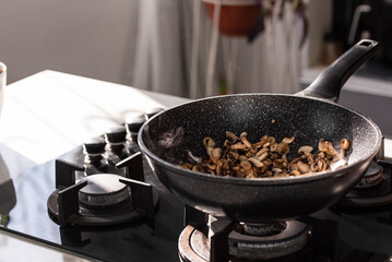 Close up of professional Chef cook hands roasts champignons mushrooms with cream in wok pan for Mediterranean cuisine. 