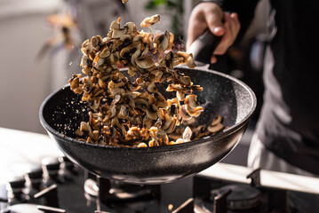 Close up of professional Chef cook hands roasts champignons with cream in wok pan for Mediterranean cuisine. Flying mushrooms in motion levitation. 