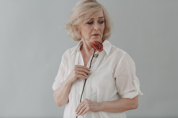 Upset elderly woman in white dressed hold withered single one dry old rose flower