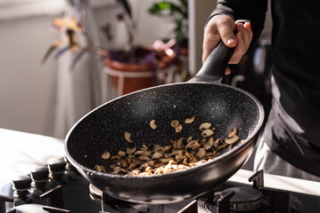 Close up of professional Chef cook hands roasts champignons with cream in wok pan for Mediterranean cuisine. Flying mushrooms in motion levitation. 