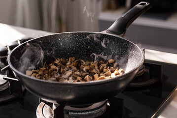 Close up of professional Chef cook hands roasts champignons mushrooms with cream in wok pan for Mediterranean cuisine. 