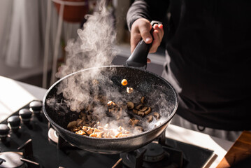 Close up of professional Chef cook hands roasts champignons with cream in wok pan for Mediterranean cuisine. Flying mushrooms in motion levitation. 