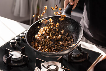 Close up of professional Chef cook hands roasts champignons with cream in wok pan for Mediterranean cuisine. Flying mushrooms in motion levitation. 
