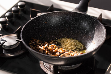 Close up of professional Chef cook hands roasts champignons mushrooms with cream in wok pan for Mediterranean cuisine. 