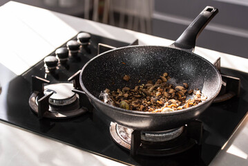 Close up of professional Chef cook hands roasts champignons mushrooms with cream in wok pan for Mediterranean cuisine. 