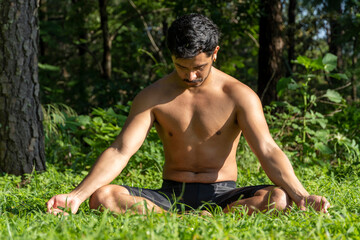 Naklejka na ściany i meble hispanic and latin man, meditating in the middle of a forest, receiving sun rays, brown skin, mexico