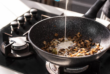 Close up of professional Chef cook hands roasts champignons mushrooms with cream in wok pan for Mediterranean cuisine. 