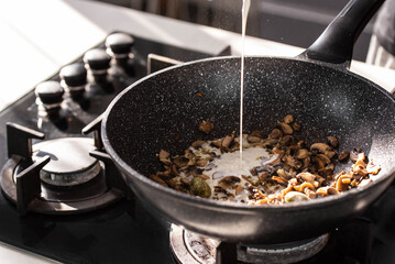 Close up of professional Chef cook hands roasts champignons mushrooms with cream in wok pan for Mediterranean cuisine. 
