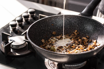 Close up of professional Chef cook hands roasts champignons mushrooms with cream in wok pan for...