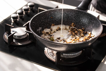 Close up of professional Chef cook hands roasts champignons mushrooms with cream in wok pan for Mediterranean cuisine. 