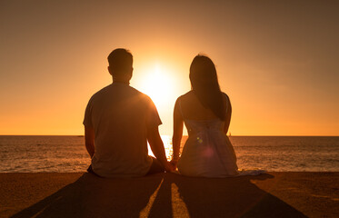 Couple sitting watching the ocean sunset holding hands. People enjoying nature. 