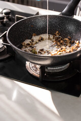 Close up of professional Chef cook hands roasts champignons mushrooms with cream in wok pan for Mediterranean cuisine. 