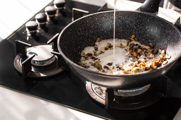 Close up of professional Chef cook hands roasts champignons mushrooms with cream in wok pan for Mediterranean cuisine. 