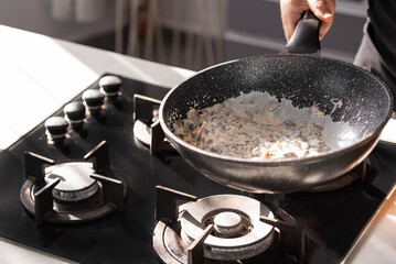 Close up of professional Chef cook hands roasts champignons mushrooms with cream in wok pan for Mediterranean cuisine. 