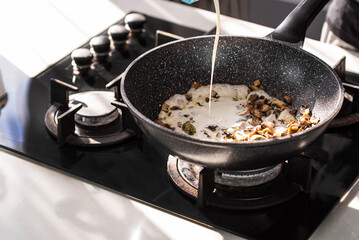 Close up of professional Chef cook hands roasts champignons mushrooms with cream in wok pan for Mediterranean cuisine. 