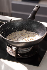 Close up of professional Chef cook hands roasts champignons mushrooms with cream in wok pan for Mediterranean cuisine. 