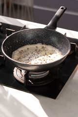 Close up of professional Chef cook hands roasts champignons mushrooms with cream in wok pan for Mediterranean cuisine. 