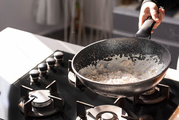 Close up of professional Chef cook hands roasts champignons mushrooms with cream in wok pan for Mediterranean cuisine. 
