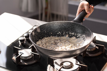 Close up of professional Chef cook hands roasts champignons mushrooms with cream in wok pan for Mediterranean cuisine. 