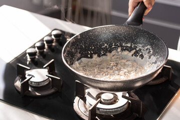 Close up of professional Chef cook hands roasts champignons mushrooms with cream in wok pan for Mediterranean cuisine. 