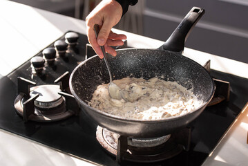 Close up of professional Chef cook hands roasts champignons mushrooms with cream in wok pan for Mediterranean cuisine. 
