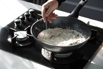 Close up of professional Chef cook hands roasts champignons mushrooms with cream in wok pan for Mediterranean cuisine. 
