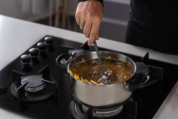 Professional chef cook making Italian Tagliatelle spaghetti pasta with at modern kitchen gas stove in pot. Boiling water. 
