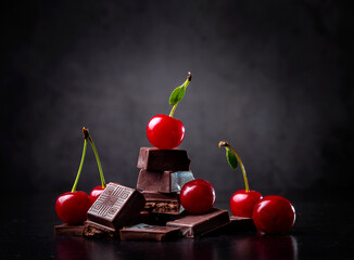 Pieces of dark chocolate and fresh cherry on a dark background. Copy space