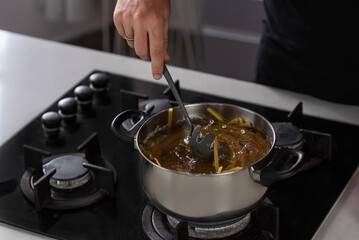 Professional chef cook making Italian Tagliatelle spaghetti pasta with at modern kitchen gas stove in pot. Boiling water. 