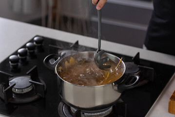 Professional chef cook making Italian Tagliatelle spaghetti pasta with at modern kitchen gas stove in pot. Boiling water. 