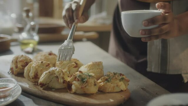 Cropped shot of unrecognizable black woman brushing garlic butter on top of freshly baked bread buns