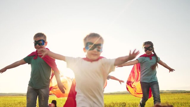 team of kids superheroes run. happy family kid concept. a group of children playing superheroes in capes and masks run through the grass at sunset. success dream business striving for goal concept