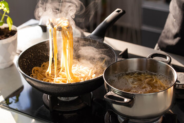 Professional chef cook making Italian Tagliatelle pasta with mushrooms and cream at modern kitchen gas stove in wok pan and pot.