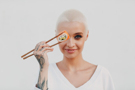 Portrait Of Young Smiling Millenial European Short Haired Woman Eating Sushi Philadelphia Salmon Roll . Beautiful Happy Blonde Girl Outdoor.