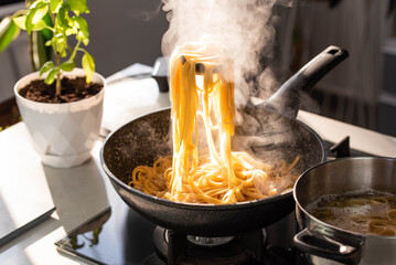 Professional chef cook making Italian Tagliatelle pasta with mushrooms and cream at modern kitchen gas stove in wok pan and pot.
