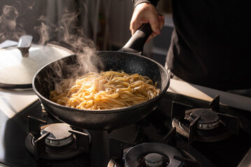 Professional chef cook making vegetarian Italian Tagliatelle pasta with mushrooms and cream at modern kitchen gas stove in wok pan.