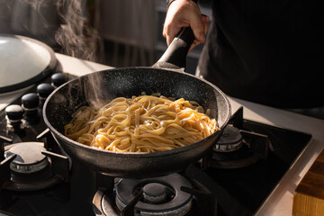Professional chef cook making vegetarian Italian Tagliatelle pasta with mushrooms and cream at modern kitchen gas stove in wok pan.