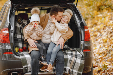 Father and his children sitting at open trunk of hatchback car in autumn forest