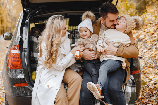 Young Family Sitting At Open Trunk Of Hatchback Car In Autumn Forest