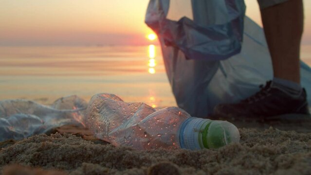 Man volunteer collects plastic on the beach close-up. Volunteers collect garbage in a garbage bag. Plastic pollution and environmental problems concept. Greening the planet