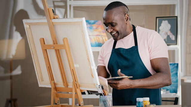 Side view happy smiling cheerful creative talented inspired old African American senior man artist male painter in apron drawing painting picture creative idea on canvas in art studio school paints - Powered by Adobe