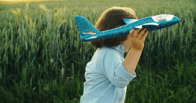 Happy boy throwing paper plane running in the field on sunny day. Child's play, fantasy and dream. High quality 4k footage